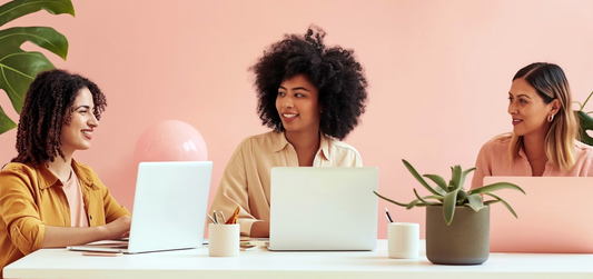 Three diverse female entrepreneurs engaging in a collaborative discussion at a modern workspace, with laptops and a plant on the table