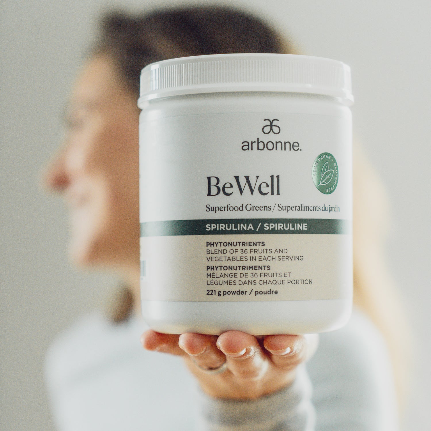 Smiling person presenting Arbonne BeWell Superfood Greens container with focus on the product label.