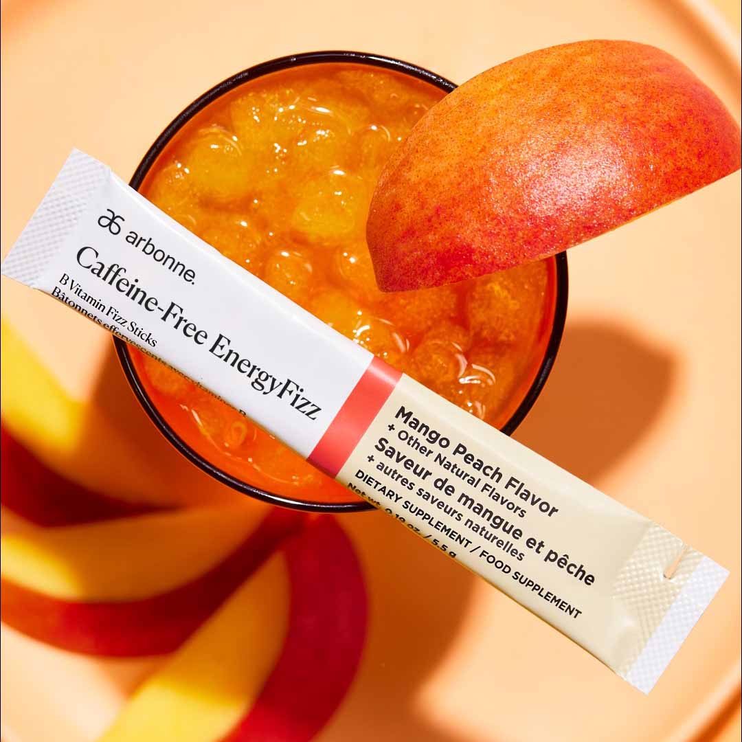 Arbonne Caffeine-Free EnergyFizz B Vitamin Fizz Stick in mango peach flavor displayed with a glass of orange beverage and peach slices.