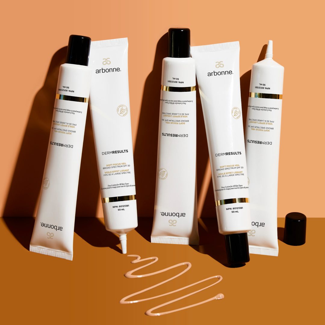 Arbonne DermResults products displayed on an orange background. The image shows multiple tubes of the product, with one tube partially squeezed, showcasing the product texture.