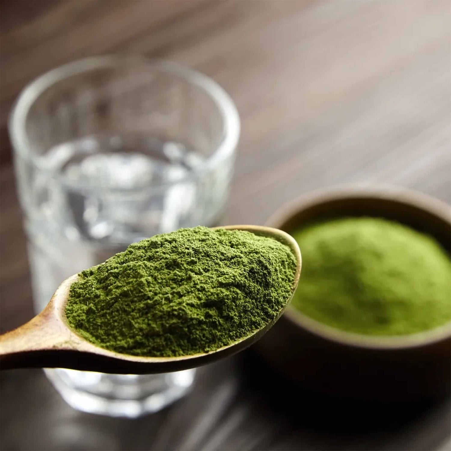A spoonful of Arbonne Greens powder with a glass of water in the background, showcasing the Green Gut Glow energy supplement for mind, body, and skin.