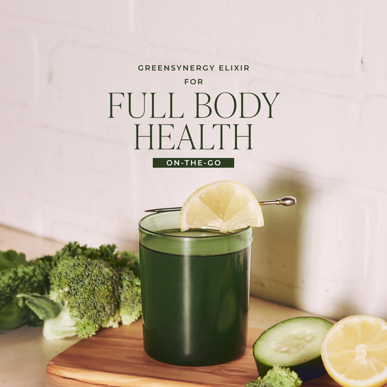 Arbonne GreenSynergy Elixir glass garnished with a lemon slice on a wooden board with broccoli and cucumber, with the text "GreenSynergy Elixir for Full Body Health On-The-Go" in the background.