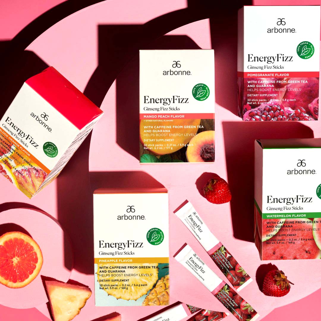 Assorted flavors of Arbonne EnergyFizz Ginseng Fizz Sticks displayed on a pink background with fresh fruit.