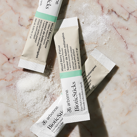 Arbonne BioSticks dietary supplement packets scattered on a marble surface with product powder spilling out.