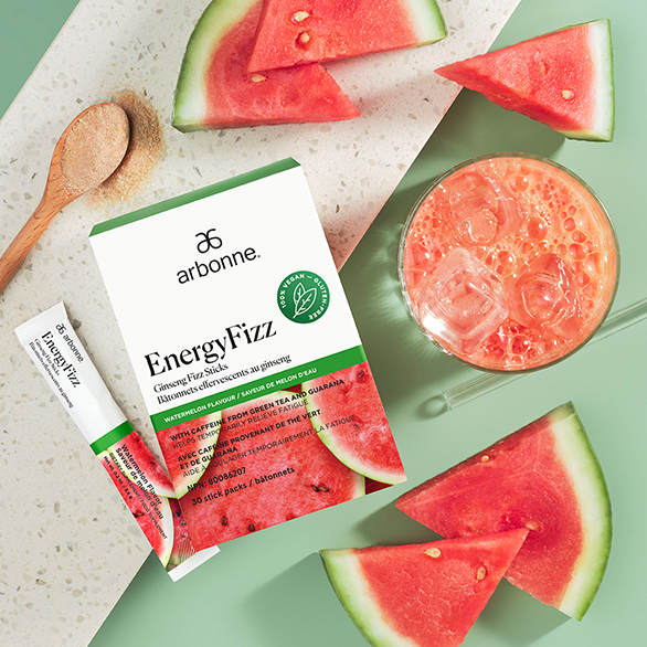 Arbonne EnergyFizz Ginseng Fizz Sticks with a refreshing watermelon-flavored drink surrounded by fresh watermelon slices on a green surface.