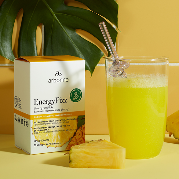 Arbonne EnergyFizz Ginseng Fizz Sticks in pineapple flavor with a glass of fizzy drink and fresh pineapple on a yellow background.