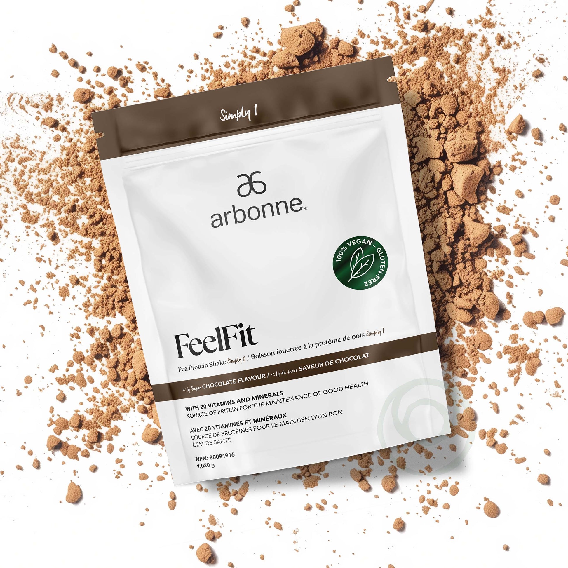 Arbonne FeelFit chocolate-flavored pea protein shake powder with 20 vitamins and minerals, in a white and brown package, surrounded by scattered chocolate powder.