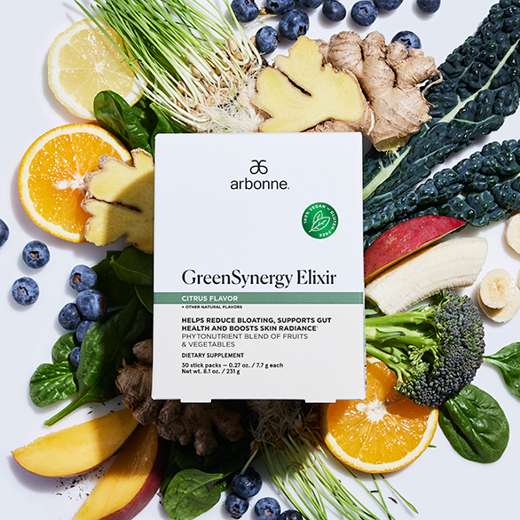 Arbonne GreenSynergy Elixir box surrounded by fresh fruits, vegetables, and herbs, including oranges, ginger, blueberries, kale, and bananas.