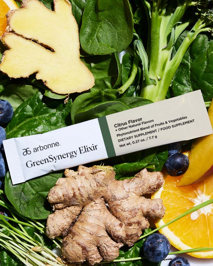 Arbonne GreenSynergy Elixir packet placed on fresh spinach leaves, ginger root, oranges, and blueberries.