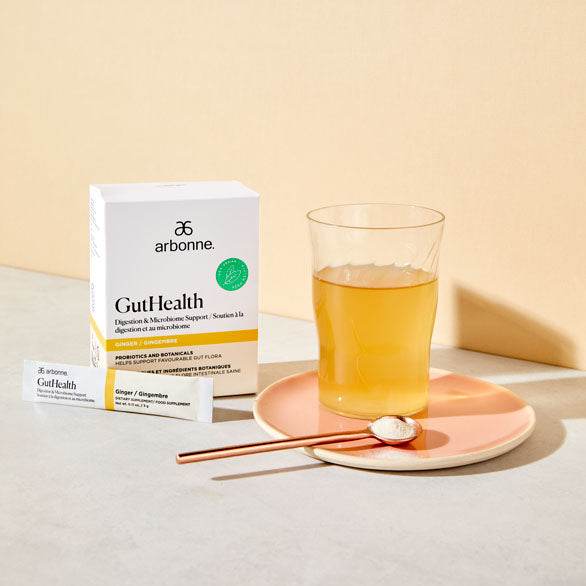 Arbonne GutHealth product box next to a glass of digestive support beverage on a peach-colored plate, with a natural light background.