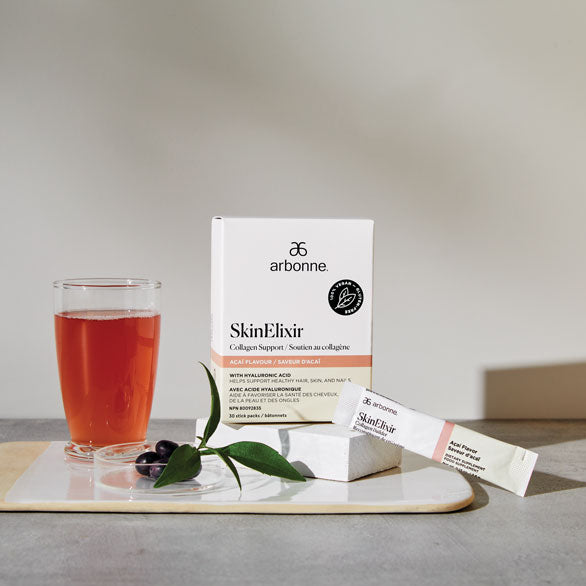Arbonne SkinElixir Collagen Support with a glass of the prepared drink and sachet on a modern kitchen counter.