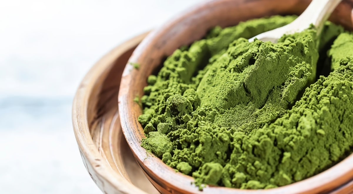 Close-up of vibrant green chlorella powder in a wooden bowl with a wooden spoon.