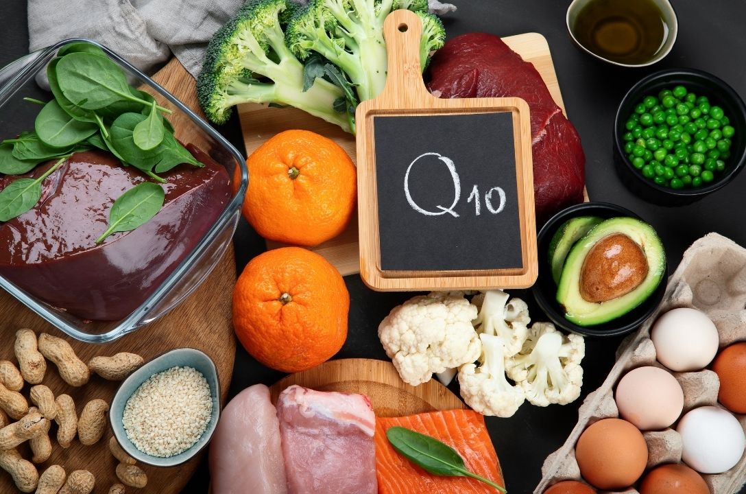 Variety of foods rich in Coenzyme Q10, including beef liver, broccoli, spinach, oranges, avocado, salmon, eggs, and nuts, displayed with a chalkboard labeled "Q10."