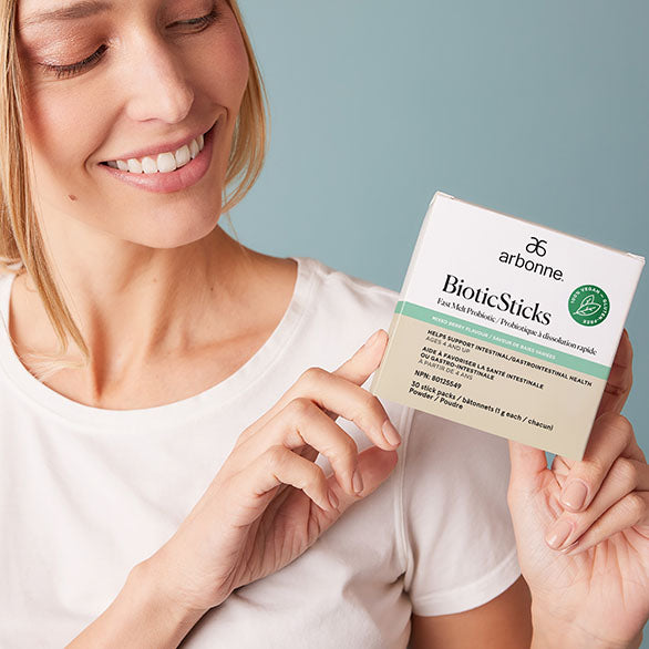 Happy woman holding Arbonne BioticSticks, showcasing the product's packaging focused on gut health and probiotics.