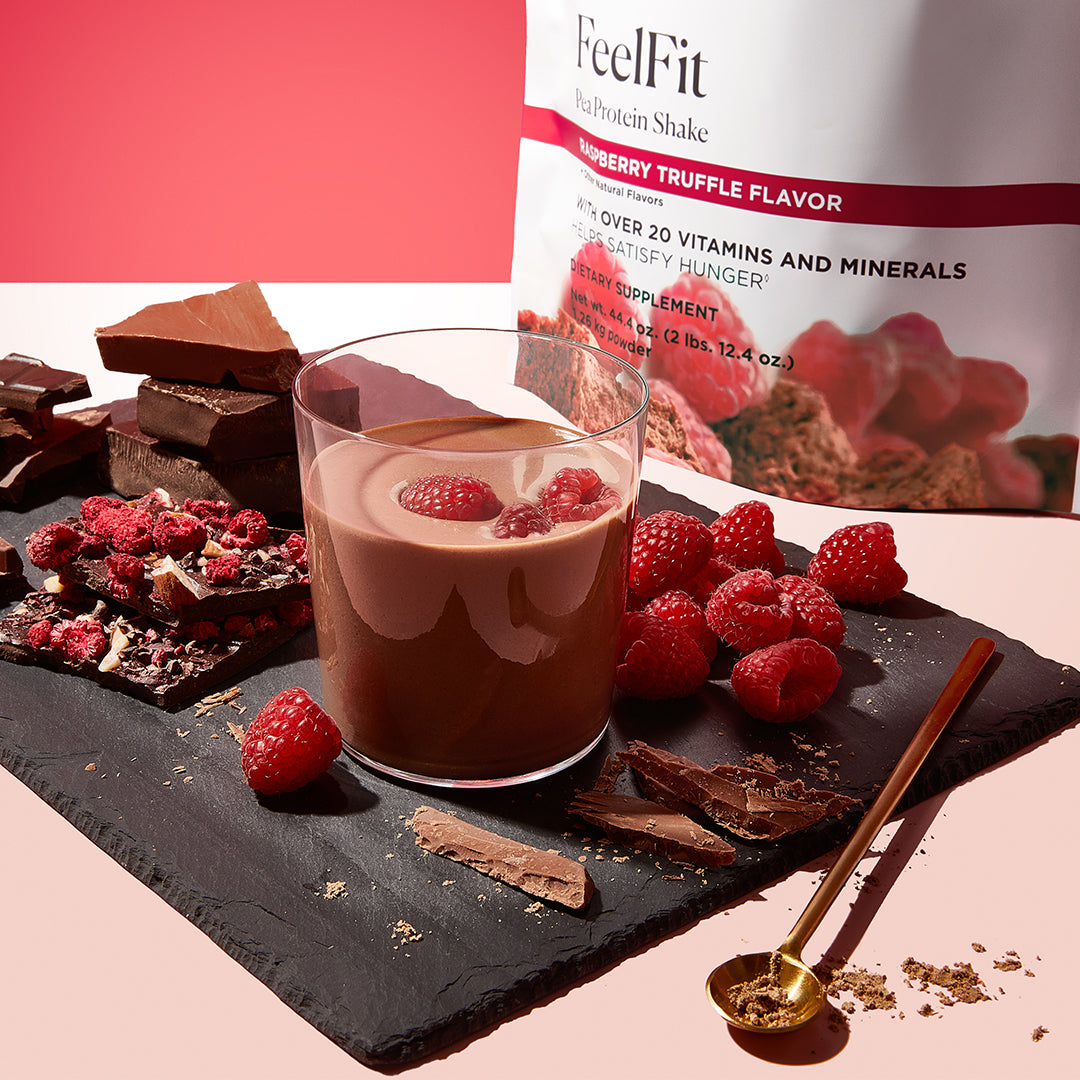 Raspberry Truffle flavored FeelFit pea protein shake with raspberries and chocolate pieces on a slate board.