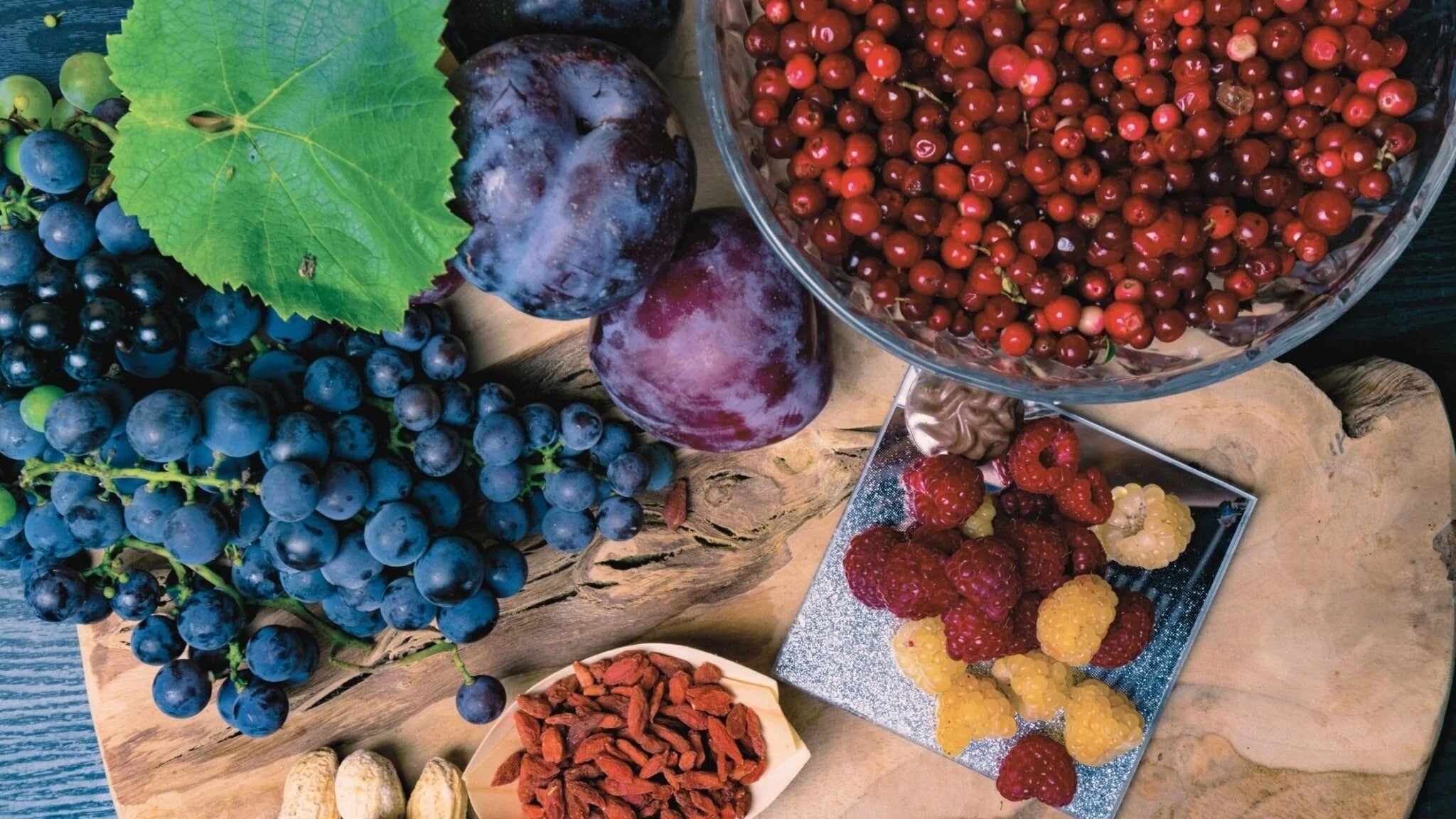 Assortment of colorful berries and fruits rich in resveratrol, including grapes, plums, cranberries, raspberries, and goji berries arranged on a wooden surface