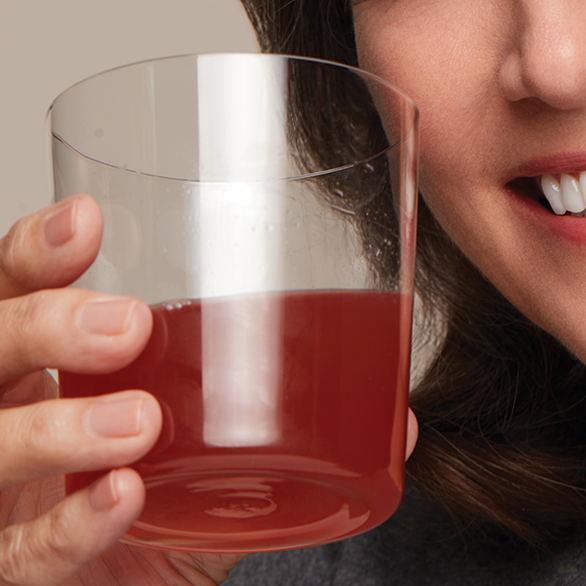 Smiling woman holding a clear glass with a red nutritional drink.